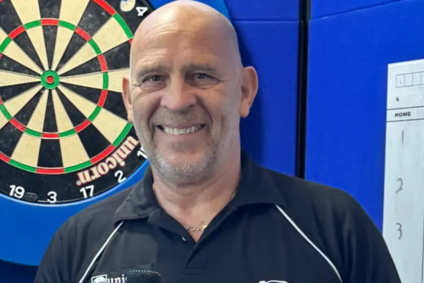 Russ Bray standing and smile with a dart board in the background